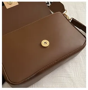 Detail of the magnetic buckle closure on a brown matte leather bag with patterned strap