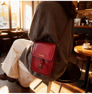 Détail d'un mini sac téléphone rouge foncé avec imprimé doré et nœud dans un café