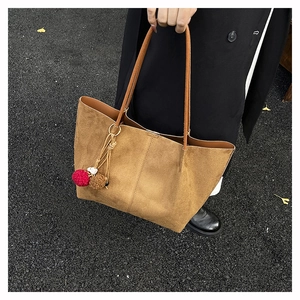 Detail of tan suede tote bag with long handles and a colorful plush pom-pom charm