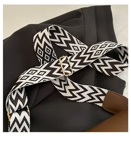 Close-up of a wide woven shoulder strap with black and white geometric patterns and gold buckle