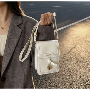 Détail d'un mini sac pour téléphone en cuir verni blanc avec pendentif doré et ruban