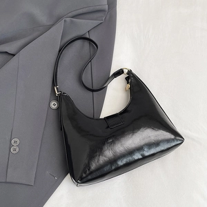 Minimalist black patent leather hobo bag with adjustable strap on white fabric background