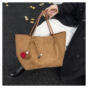 Detail of suede tote bag with brown pompom and bead charm on autumn leaf background