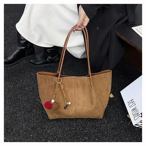 Detail of dark brown suede tote bag featuring a decorative pom-pom and knotted tassel charm