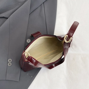 Minimalist burgundy patent leather shoulder bag with glossy finish and gold hardware buckle