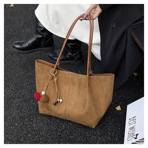 Detail of a brown frosted tote bag with a decorative tassel and plush pompom charm