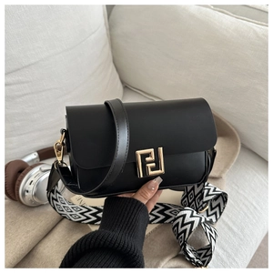 Detail of matte black crossbody square bag with gold geometric lock and patterned strap