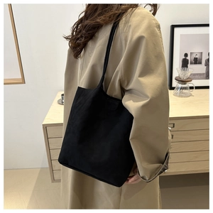 Detailed side view of a large black minimalist tote bag worn by a person in a cozy interior