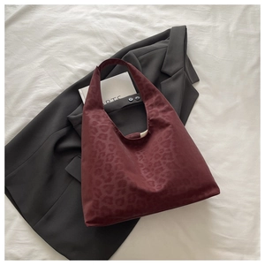 Macro detail of wine red leopard print velvet tote bag on a black blazer backdrop