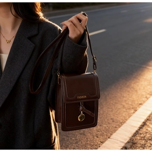 Gros plan d'un mini sac à bandoulière marron foncé vintage avec pendentif doré au coucher du soleil