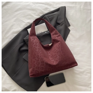 Detailed view of dark red leopard print tote bag on a textured fabric background