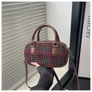 Detail of checkered crossbody bag with red and green plaid fabric and brown leather handle