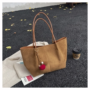 Close-up of brown frosted suede tote bag with plush charm on ginkgo leaf street