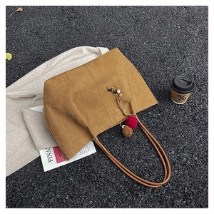 Close-up of brown suede tote bag with decorative tassel charms on an urban pavement