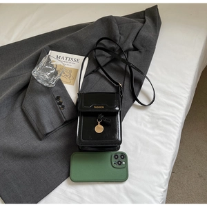 Détail du petit sac carré en cuir verni noir avec breloque dorée sur une veste grise