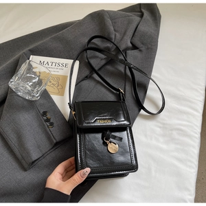 Détail du petit sac carré noir verni avec lettrage doré posé sur une veste de costume chic