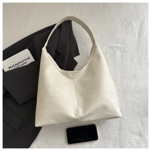Détail du grand sac hobo crème en cuir texturé sur fond de tissu blanc épuré
