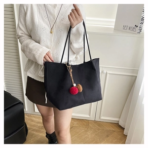 Detail of black suede tote bag with decorative dual-tone pompom and slim shoulder straps