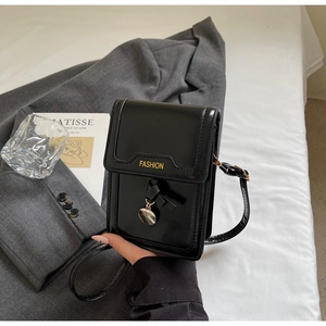 Détail du sac à bandoulière en cuir verni noir avec texte jaune et pendentif doré