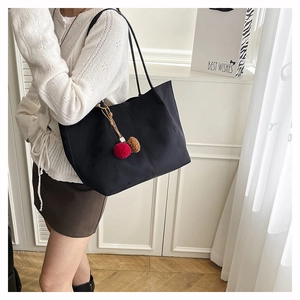 Close-up of black matte tote bag with dual-tone pompom charm in a lifestyle setting