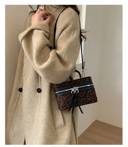 Détail du sac boîte léopard avec double fermeture éclair et pompons noirs sur manteau