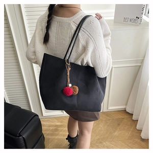 Detail of black suede tote bag with dual-tone plush ball charm on back-view model