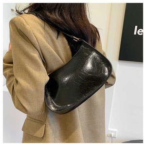 Close-up of black glossy oil wax leather shoulder bag with golden buckle on model