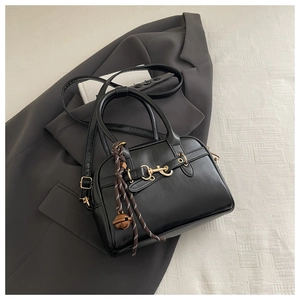Close-up of black leather shell bag with golden horse-bit hardware and charm details