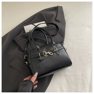 Detail of black leather Boston bag with gold horsebit hardware on a grey blazer