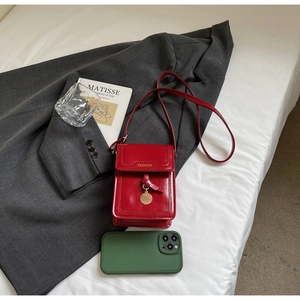 Détail du petit sac carré en cuir rouge brillant avec texte doré et pendentif en métal