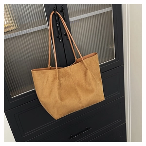 Detail of caramel suede tote bag with dual slim straps hanging on a modern cabinet door