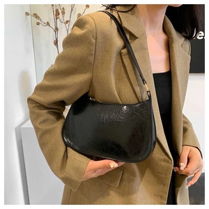 Close-up of black glossy baguette bag with metal zipper worn with a brown blazer