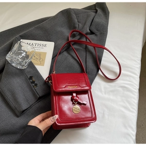Détail du petit sac bandoulière rouge foncé avec lettrage fashion doré sur le rabat