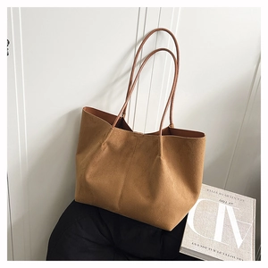 Close-up of caramel suede tote bag with slim shoulder straps on a textured cushion