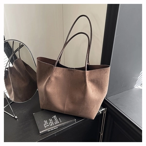 Detail of a brown matte suede tote bag placed on a black table with decor and soft lighting