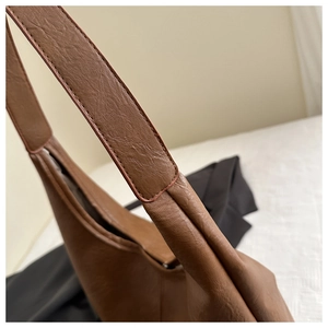 Gros plan sur la texture du cuir marron foncé et les coutures de la bandoulière