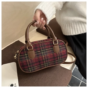Detail of red plaid Boston bag with leather straps and gold hardware in cozy home setting
