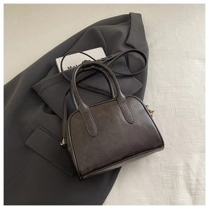 Detail of dark brown leather Boston bag with vintage texture placed on a grey blazer