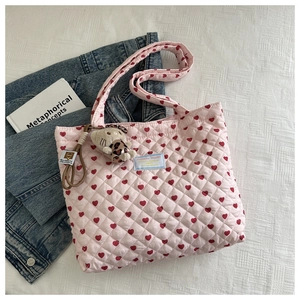 Pink quilted tote bag with red hearts and a cute plush cat charm on a white bed