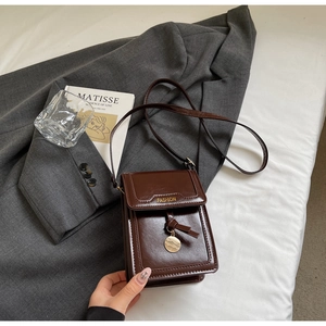 Détail du petit sac bandoulière en cuir marron avec pendentif doré sur blazer gris