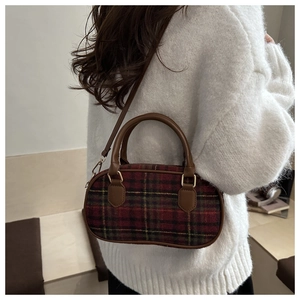 Detail of red and black plaid crossbody bag with brown leather strap on white sweater
