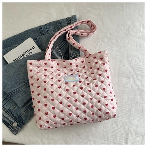 Close-up of pink quilted tote bag with red heart pattern and brand label detail