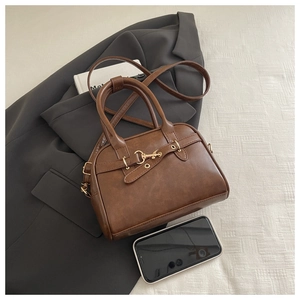 Detail of brown vintage crossbody bag with gold horsebit buckle and faux leather texture