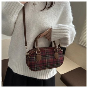 Close-up of vintage red and green plaid handbag featuring brown leather handles and gold hardware