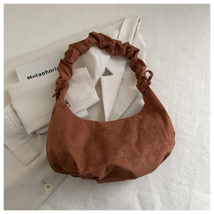 Détail du sac croissant en daim marron avec anse froncée sur un blazer élégant