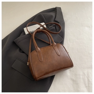 Detailed view of a vintage brown Boston handbag with dual handles on a grey blazer