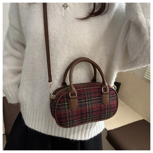 Close-up of red and green plaid handbag with brown leather handles and gold metal accents