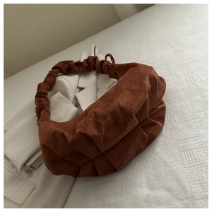 Gros plan du sac nuage plissé en daim marron sur literie blanche avec un blazer