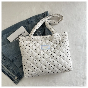 Flat lay of white quilted tote bag with black heart patterns and light blue label