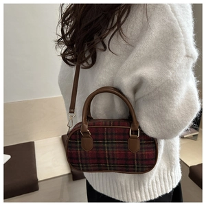 Close-up of red plaid bowling bag with brown leather handles on white knit sweater